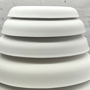 May include: A set of five white ceramic bowls stacked on top of each other. The bowls are all the same shape and size, and they have a smooth, rounded edge.