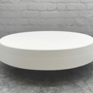 May include: White ceramic round pedestal with a slightly raised edge. The pedestal is smooth and has a matte finish.
