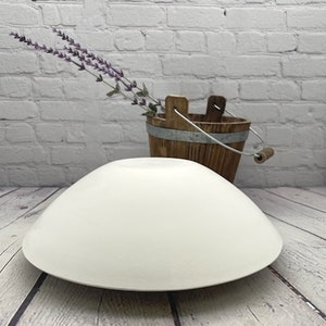 May include: White ceramic bowl with a wide, shallow shape. The bowl is sitting on a wooden surface.