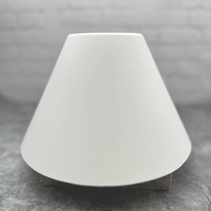 May include: A white lampshade with a conical shape. The lampshade is sitting on a gray surface.
