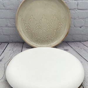 May include: Two ceramic plates, one with a white glaze and the other with a cream glaze and a raised floral design.