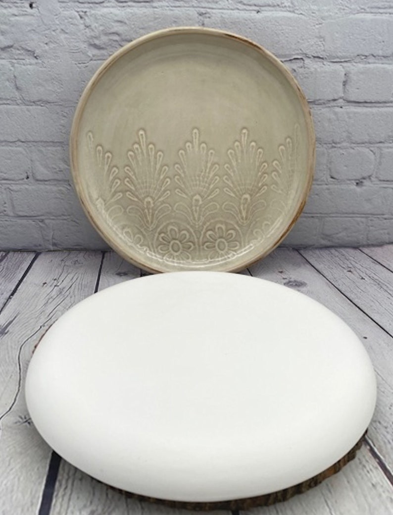 May include: Two ceramic plates, one with a white glaze and the other with a cream glaze and a raised floral design.
