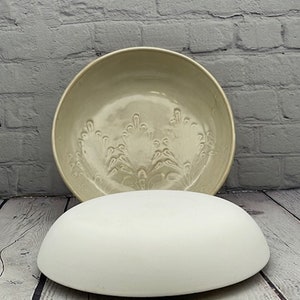 May include: A white ceramic bowl with a raised floral design. The bowl is sitting on a white ceramic pedestal.
