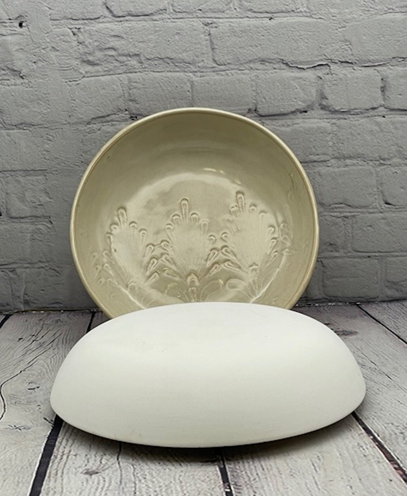 May include: A white ceramic bowl with a raised floral design. The bowl is sitting on a white ceramic pedestal.