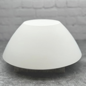 May include: A white ceramic cake stand with a wide, shallow base and a gently sloping, rounded top. The stand is designed for displaying cakes, pastries, or other desserts.