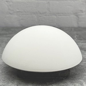 May include: A white, dome-shaped lamp with a smooth, rounded surface. The lamp is sitting on a gray surface.