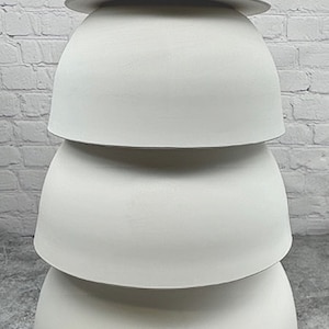May include: A stack of four white, semi-spherical decorative objects. Each piece is a different size, with the largest at the bottom and the smallest at the top. The objects are arranged to create a tower-like structure. The background is a white brick wall.