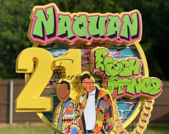 以下が含まれることがあります： 「Naquan」という名前が落書き風の緑と黄色のケーキトッパーで、「21」という数字が黄色で書かれています。トッパーには、「ベルエアのフレッシュプリンス」の映画の登場人物2人のグラフィックと金色のチェーンも付いています。