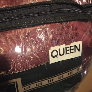 May include: A dark burgundy bedding set packaged in a clear plastic zippered bag. The fabric features a gold floral pattern. A white label on the front of the packaging displays the text QUEEN in black letters, with the repeated text UHF below it.