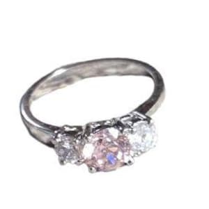 May include: A silver ring with three clear, round-cut gemstones. The center stone is a light pink color, flanked by two smaller, clear stones. The ring is set against a plain white background.