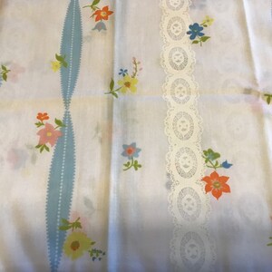 May include: White fabric with a blue and white striped pattern and a white lace trim. The fabric is decorated with a floral pattern in shades of pink, orange, yellow, and blue.