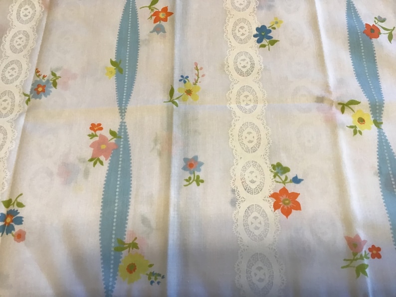 May include: White fabric with a blue and white striped pattern and a white lace trim. The fabric is decorated with a floral pattern in shades of pink, orange, yellow, and blue.
