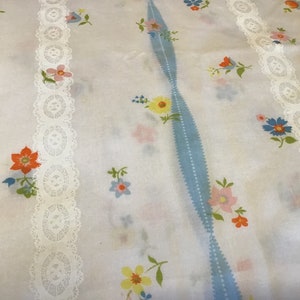 May include: White fabric with a blue and white striped pattern and white lace trim. The fabric is covered in a small floral print with pink, yellow, orange, and blue flowers.