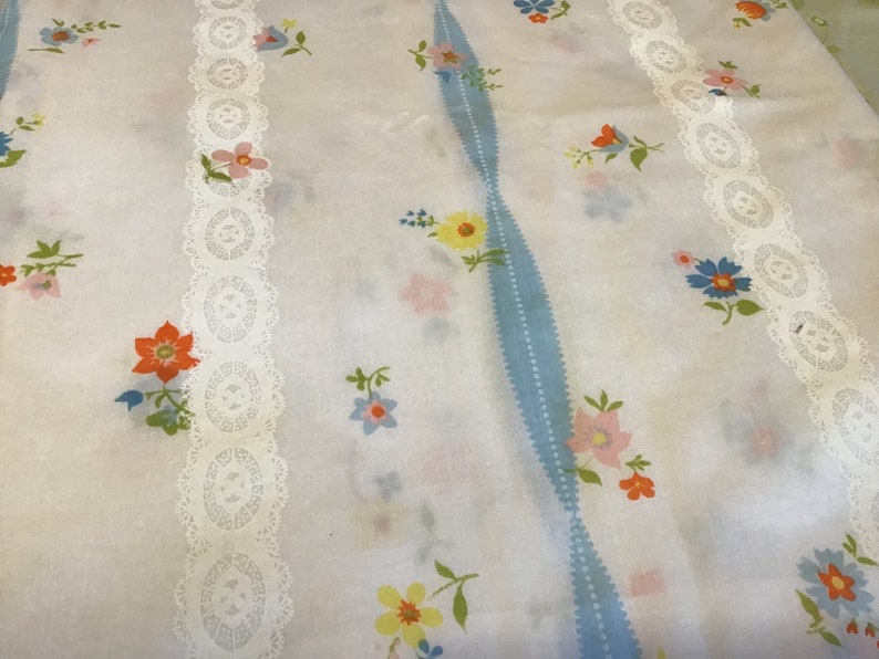 May include: White fabric with a blue and white striped pattern and white lace trim. The fabric is covered in a small floral print with pink, yellow, orange, and blue flowers.