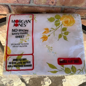 May include: A packaged double flat sheet by Morgan Jones. The white sheet features a floral pattern with yellow roses and green leaves. The packaging includes text that reads "No-Iron luxury muslin SHEET" and is designed for a 54 in. x 76 in. mattress.
