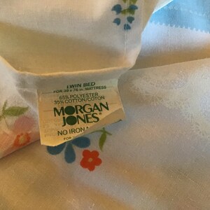 May include: A white twin bed sheet with a floral pattern in shades of pink, blue, and green. The sheet has a label that reads "I Win Bed for 39 x 76 in. Mattress 65% Polyester 35% Cotton/Coton Morgan Jones No Iron For"