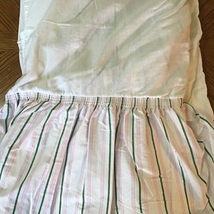 May include: White bed skirt with a pink and green striped ruffle. The ruffle has a gathered elastic band.