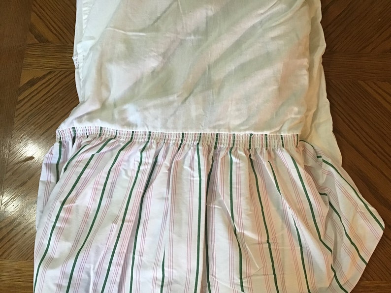 May include: White bed skirt with a pink and green striped ruffle. The ruffle has a gathered elastic band.