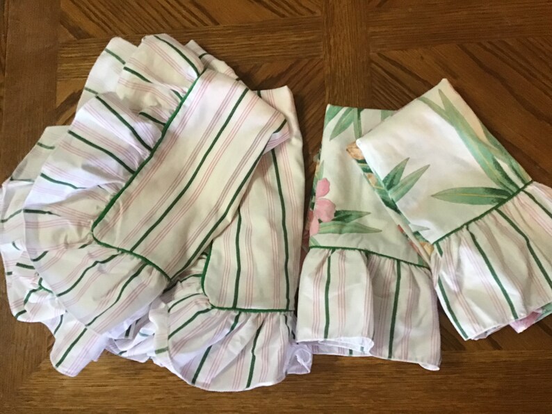 May include: Three pillowcases with green and pink stripes and a floral print. The pillowcases have a ruffled edge and are trimmed with green.