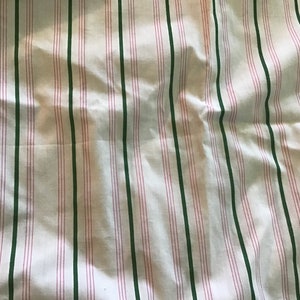 May include: White fabric with green and pink stripes. The fabric is wrinkled and has a soft texture.