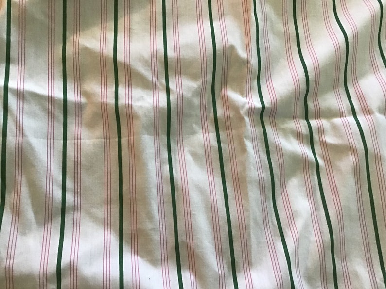 May include: White fabric with green and pink stripes. The fabric is wrinkled and has a soft texture.