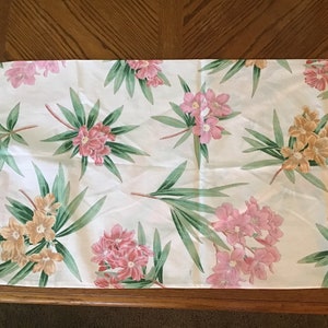 May include: A white table runner with a pink and yellow floral pattern. The runner has a ruffled edge with pink and white stripes.