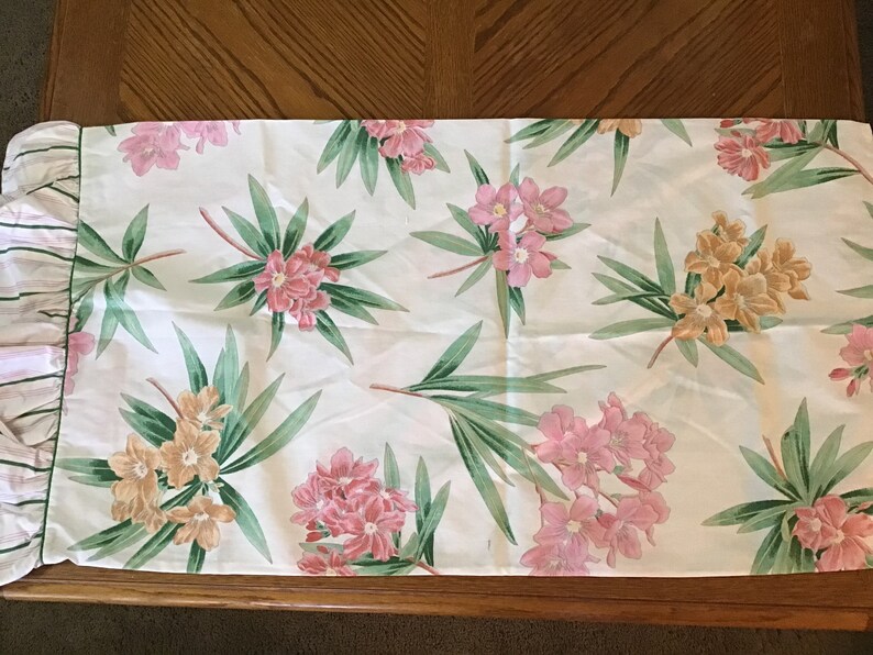 May include: A white table runner with a pink and yellow floral pattern. The runner has a ruffled edge with pink and white stripes.