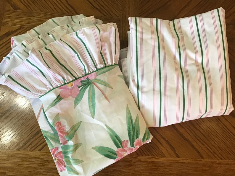 May include: Two white cotton pillowcases with green and pink stripes. One pillowcase has a ruffled edge and the other has a floral print with pink flowers and green leaves.