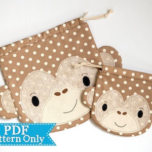 May include: Two brown fabric drawstring bags with white polka dots and a brown monkey face appliqué. The larger bag has a brown monkey face with black eyes and a white nose. The smaller bag has a brown monkey face with black eyes and a white nose. The text "PDF Pattern Only" is on a blue ribbon.
