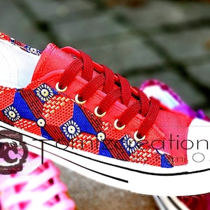 May include: Red canvas sneakers with a colourful patterned design. The pattern features red, blue and gold geometric shapes. The shoes have white laces and a white rubber sole.