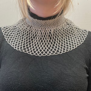 May include: A silver beaded collar necklace with a wide, open design. The necklace is made of small, round beads that are strung together in a delicate pattern.