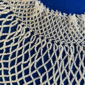 May include: A white beaded collar necklace with a delicate, intricate design. The necklace is made of small, round beads that are woven together to create a lacy pattern.