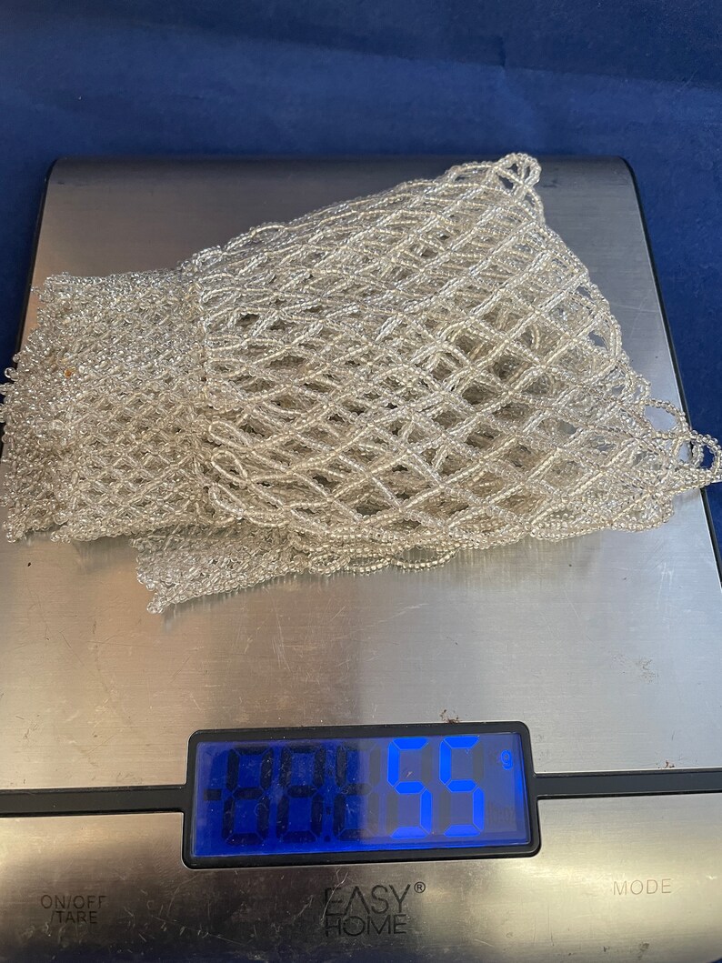 May include: A white beaded net bag on a digital scale that reads 0.0455. The scale is silver and has a black display.