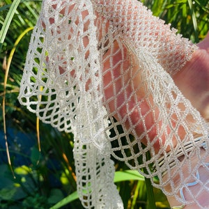 May include: A white beaded scarf with a delicate, intricate design. The scarf is made of small, white beads that are woven together to create a lacy pattern.