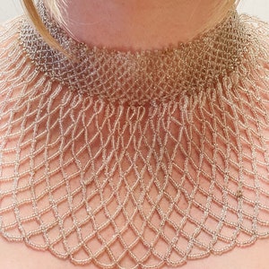 May include: A delicate, beaded choker necklace with a scalloped edge. The necklace is made of small, light brown beads woven together in a intricate pattern.