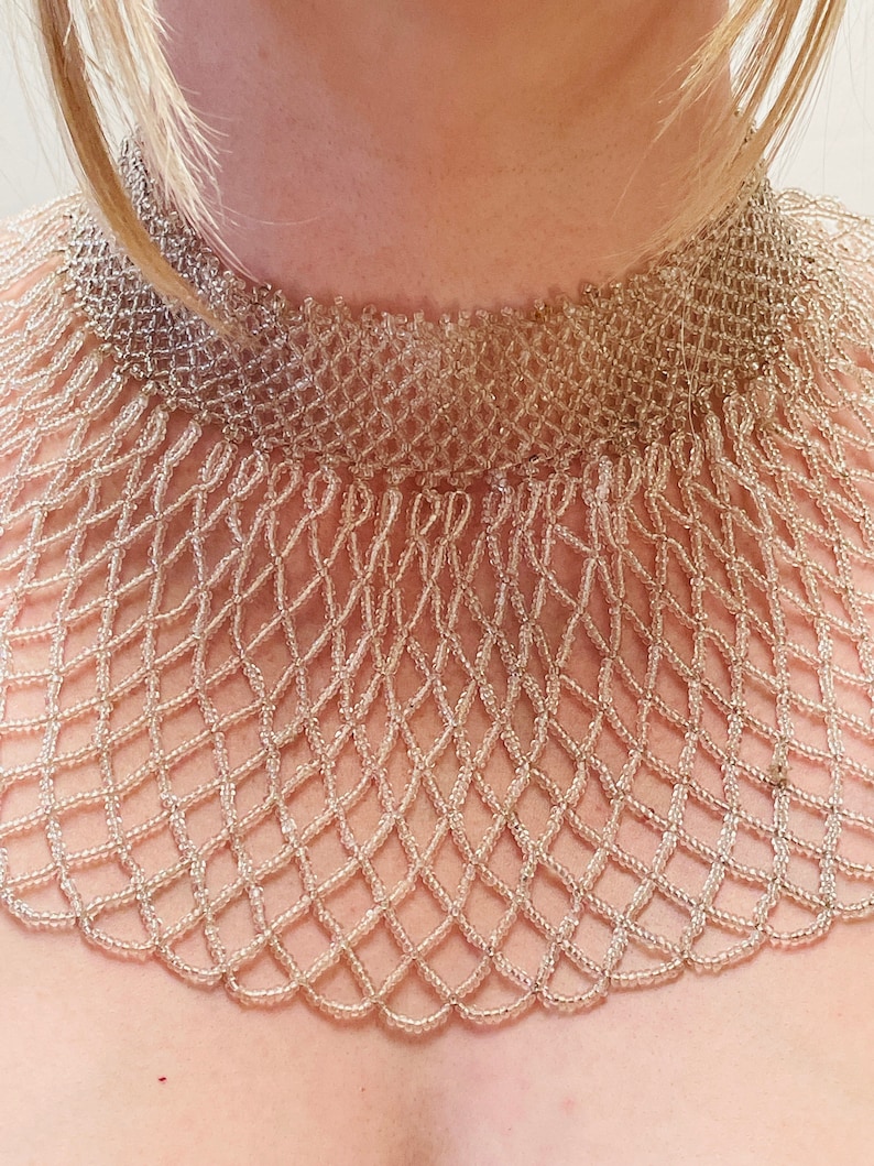 May include: A delicate, beaded choker necklace with a scalloped edge. The necklace is made of small, light brown beads woven together in a intricate pattern.