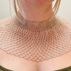 May include: A silver beaded choker necklace with a wide, fan-shaped design. The necklace is made of small, round beads that are woven together in a delicate pattern.