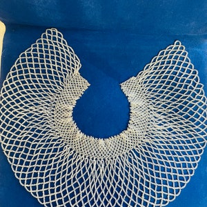 May include: A white beaded collar necklace with a delicate, intricate design. The collar is made of small, white beads woven together in a pattern that resembles a net. The collar is a traditional African accessory.