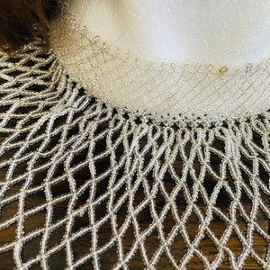 May include: A white beaded necklace with a delicate, intricate design. The necklace is made of small, round beads that are strung together in a pattern that resembles a net. The necklace is a beautiful and elegant piece of jewelry that would be perfect for a special occasion.