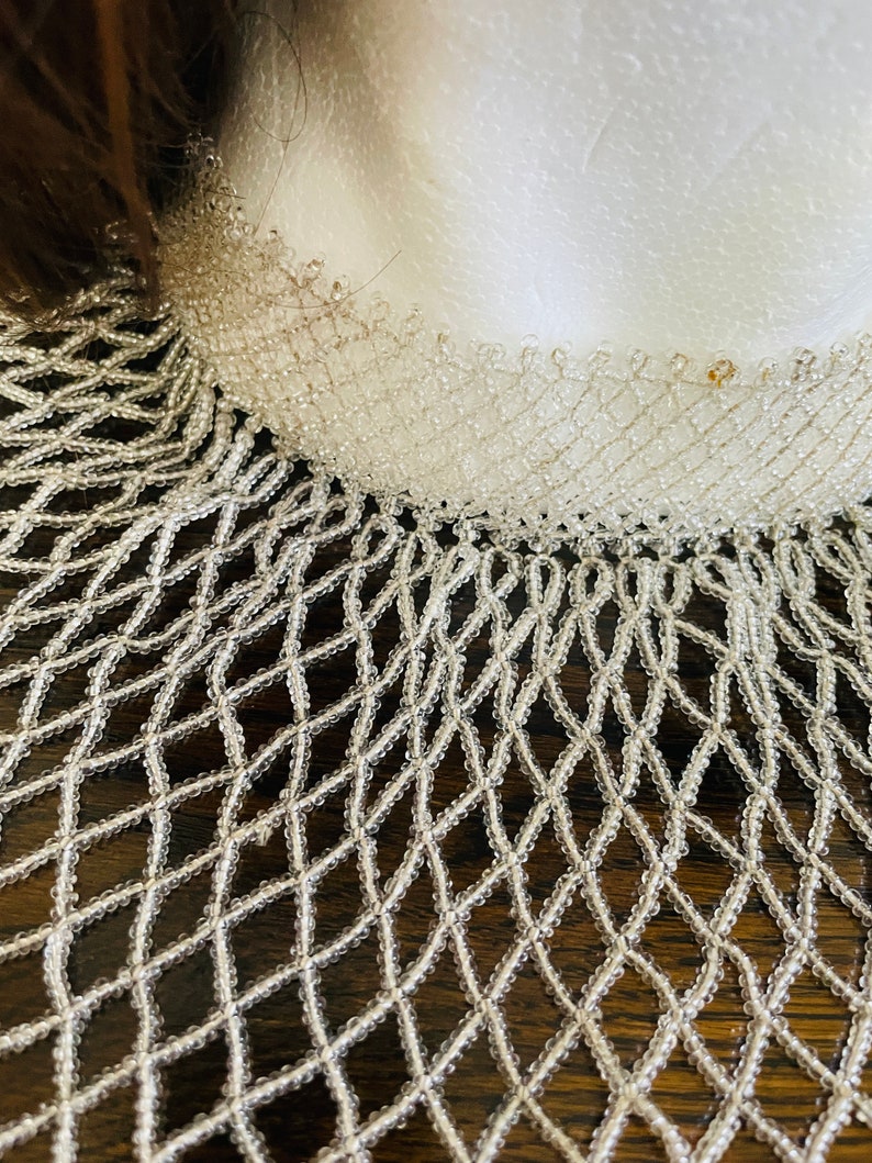 May include: A white beaded necklace with a delicate, intricate design. The necklace is made of small, round beads that are strung together in a pattern that resembles a net. The necklace is a beautiful and elegant piece of jewelry that would be perfect for a special occasion.