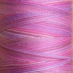 May include: A spool of pink and purple yarn with a variegated colour pattern. The yarn is wound tightly and has a smooth texture.