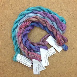 Könnte beinhalten: Fünf Spulen handgefärbter Spinnseide in Blautönen, Lila, Rosa und Türkis. Jede Spule ist mit "Spun Silk 30/2" und "30 Meter" beschriftet.