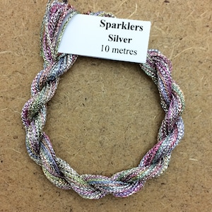 Könnte beinhalten: Eine Spule silbernen Glitzerfadens, 10 Meter lang. Der Faden ist ein mehrfarbiger Zopf aus Silber, Rosa, Grün und Blau.