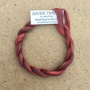 Könnte beinhalten: Ein Knäuel handgefärbter Stickgarn in Rot-, Orange- und Brauntönen. Das Garn ist mit "Oliver Twist by Jean Oliver Hand dyed in the UK not guaranteed colourfast." beschriftet.