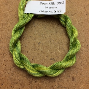 Könnte beinhalten: Ein Knäuel grüner und gelber Spinnseide, beschriftet mit "Spun Silk 30/2, 30 Meter, Colour No. S 82".