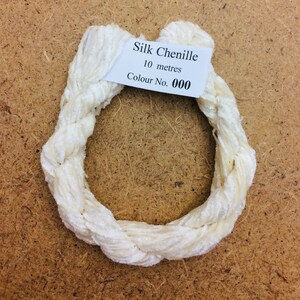 Op de afbeelding: Witte zijden chenille garen, 10 meter lang, in een cirkelvorm. Het label vermeldt "Silk Chenille 10 metres Colour No. 000".