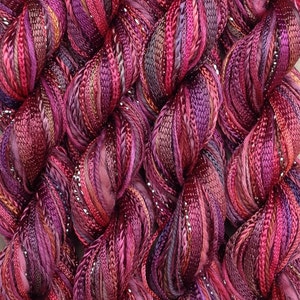 May include: Close-up of a bundle of multi-colored yarn with silver glitter thread. The yarn is a mix of deep purple, burgundy, and pink shades.