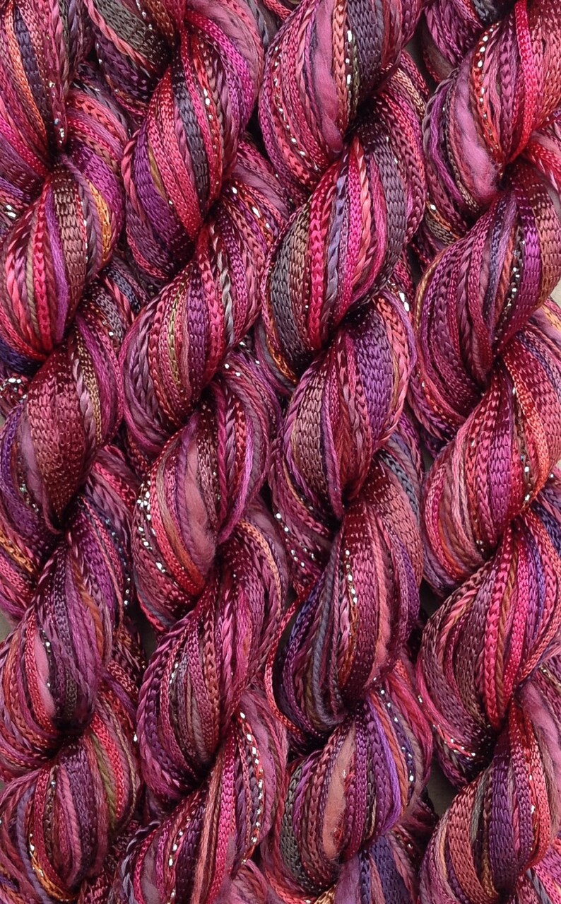 May include: Close-up of a bundle of multi-colored yarn with silver glitter thread. The yarn is a mix of deep purple, burgundy, and pink shades.