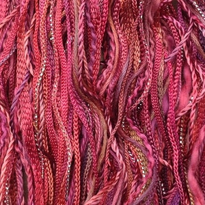 May include: A close-up of a bundle of colorful embroidery floss in shades of pink, red, and purple. The floss is made of a variety of materials, including silk, cotton, and metallic thread.