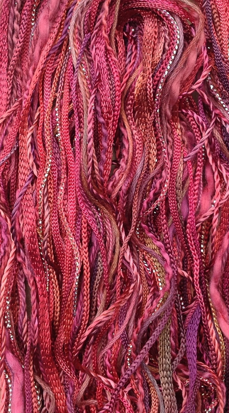May include: A close-up of a bundle of colorful embroidery floss in shades of pink, red, and purple. The floss is made of a variety of materials, including silk, cotton, and metallic thread.